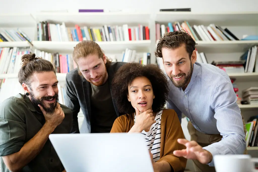 quatre collaborateurs autour d'un ordinateur avec une bibliothèque en arrière-plan, courtier courtier assurance vie luxembourg